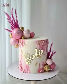 a pink and gold cake with the word barbie painted on it's side, sitting on top of a table