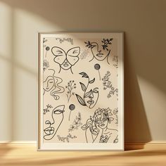 a framed art piece on a wooden floor in front of a wall with flowers and faces