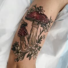 a mushroom tattoo on the arm with flowers and leaves around it's base,