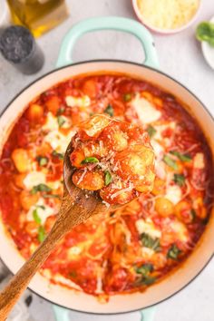 a wooden spoon full of pasta sauce with basil and cheese on top, in a blue pan