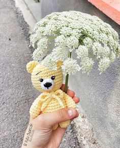 a crocheted teddy bear holding a baby's breath flower in it's hand