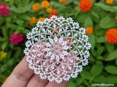 a hand holding a small white beaded brooch in front of some colorful flowers