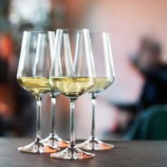 three wine glasses sitting on top of a table next to each other with white wine in them