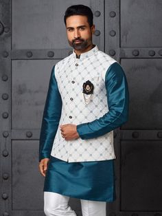 A teal blue silk kurta pajama paired with a white embroidered Nehru jacket makes for an elegant and striking outfit. The kurta, crafted from smooth silk, boasts a vibrant teal blue hue that adds a modern, refreshing twist to traditional attire. Its sleek, minimalist design allows the rich color and subtle sheen of the fabric to stand out. Complementing the kurta is a white Nehru jacket, adorned with intricate embroidery. The jacket's high collar and tailored fit exude sophistication, while the delicate, ornate embroidery adds a touch of luxury. Paired with matching silk pajama pants, this ensemble perfectly balances vibrant color and intricate detail, ideal for weddings, festivals, or formal events. COST INCLUDES NEHRU JACKET WITH KURTA PAJAMA Luxury Designer Spring Nehru Jacket, Luxury Nehru Jacket For Semi-formal Occasions, Luxury Elegant Sport Coat In Suiting Fabric, Luxury Formal Spring Nehru Jacket, Designer Silk Nehru Jacket, Luxury Raw Silk Nehru Jacket For Festive Occasions, Luxury Spring Festive Nehru Jacket, Luxury Sleek Fitted Sport Coat, Luxury Festive Nehru Jacket Front Open