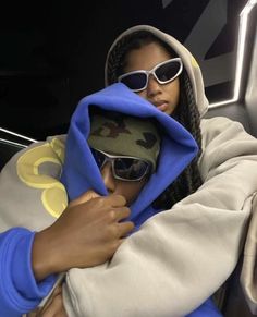 a woman wearing sunglasses and a hoodie wrapped up in a blue blanket is posing for the camera