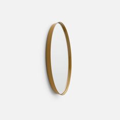 an oval mirror mounted on the wall with a gold frame and metal ring around it