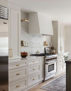 a kitchen with white cabinets and gold pulls on the oven doors, along with an area rug in front of the stove