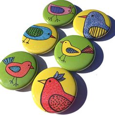 four buttons with birds painted on them are lined up in a row, one is green and the other is yellow