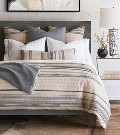 a bed with pillows and blankets on top of it next to a painting hanging above the headboard