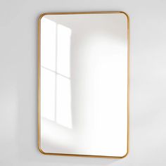 a white wall with a gold framed mirror on it and a window in the background