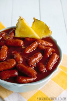 a bowl filled with hot dogs next to a slice of lemon on top of a yellow and white checkered table cloth