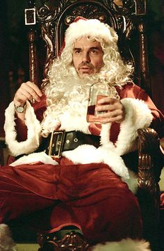 a man dressed as santa claus sitting in a chair holding a drink and looking at the camera