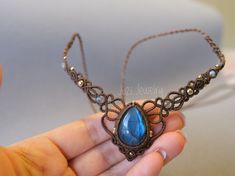 a hand holding a necklace with a blue stone in it's center and filigrees on the sides