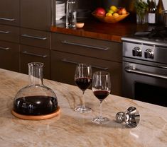 two glasses of red wine sit on a marble counter top in front of an oven