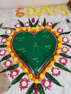 a green heart shaped sign with flowers and leaves in the shape of a flower arrangement