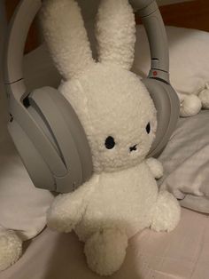 a white stuffed rabbit with headphones on it's ears sitting on a bed