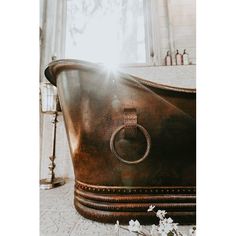 an old bathtub with a ring on the side and flowers in front of it