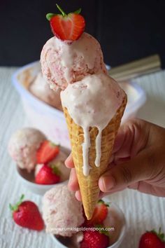 a hand holding an ice cream cone with strawberries on top and another one in the background