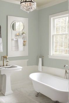 a white bath tub sitting next to a sink in a bathroom under a window with a chandelier