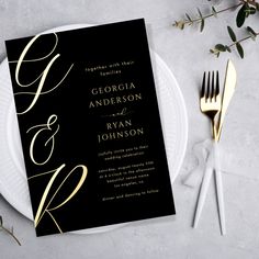 an elegant black and gold wedding card on a white plate with silverware next to it