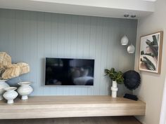 a flat screen tv sitting on top of a wooden shelf next to vases and potted plants