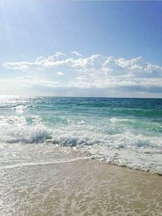 the sun shines brightly over the ocean waves on the beach, with blue sky and white clouds in the background