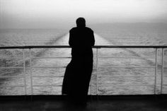 a person standing on a boat looking out at the ocean in black and white photo