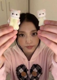 a woman holding up two small white cats on her fingers