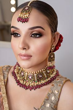 a woman wearing a red and gold necklace with matching earrings on her head is looking at the camera