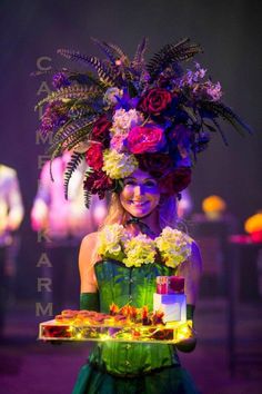 a woman in a green dress holding a tray with food on it and flowers all over her head