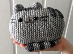 a hand holding up a crocheted gray cat shaped purse with black eyes and nose