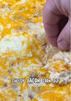 a person dipping cheese on top of a cheesy bacon corn dip