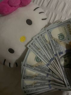 a hello kitty stuffed animal sitting on top of a pile of money