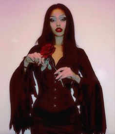 a woman with long black hair holding a red rose in her right hand and wearing dark clothing