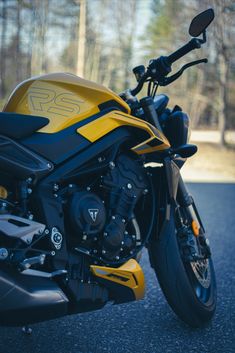 a yellow and black motorcycle parked on the side of the road with trees in the background