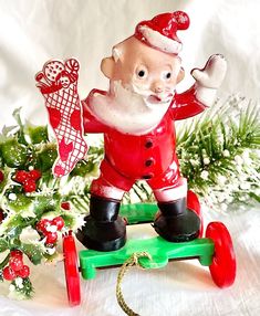 a santa clause figurine riding a green toy sleigh next to christmas decorations