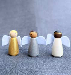 three small wooden angel figurines sitting next to each other on a gray surface