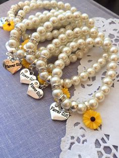 two bracelets with charms and flowers on them sitting on a lace doily next to a yellow flower