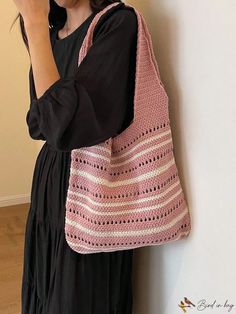 a woman standing next to a wall holding a pink crocheted bag