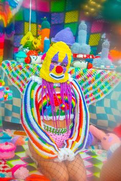 a woman wearing a clown mask sitting on top of a colorful floor covered in beads