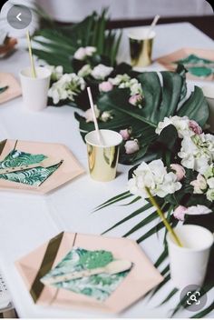 the table is set with pink and green plates, gold cups, and palm leaf napkins