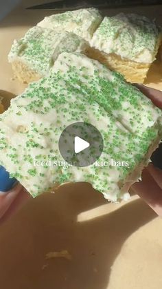 someone is holding a piece of cake with white frosting and green sprinkles