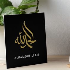 an arabic calligraphy art boarder on a table next to a potted plant