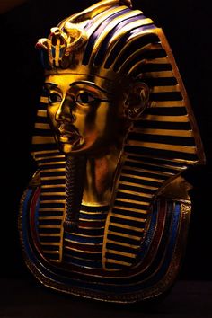 an egyptian mask with gold and blue stripes on it's face, in front of a black background