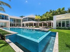 a large swimming pool in the middle of a lush green yard with lounge chairs and palm trees