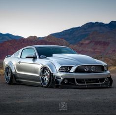 a silver mustang parked in front of mountains