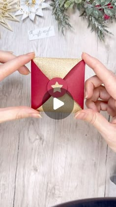 two hands holding an origami envelope over a wooden table with christmas decorations and greenery