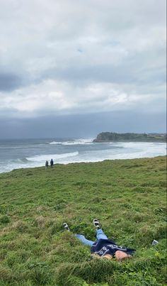 two people sitting in the grass near an ocean