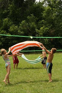 three children playing with a beach ball net on the grass in front of some trees