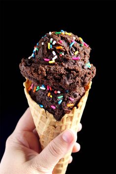 a hand holding an ice cream cone with chocolate and sprinkles